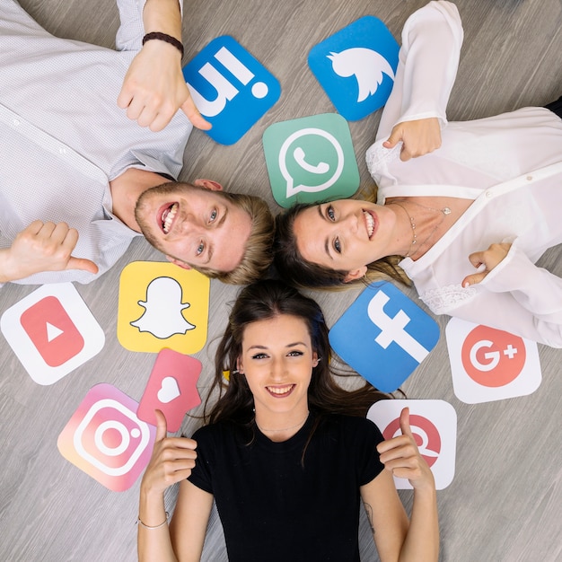 Young smiling friend lying on floor with social media logos showing thumbup sign