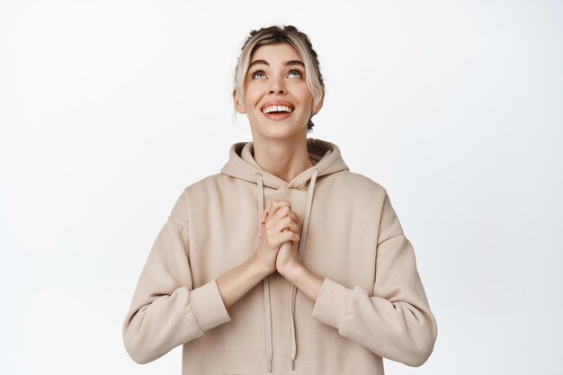 Young smiling girl hoping holding hands together and looking up while praying making wish standing hopeful against white background