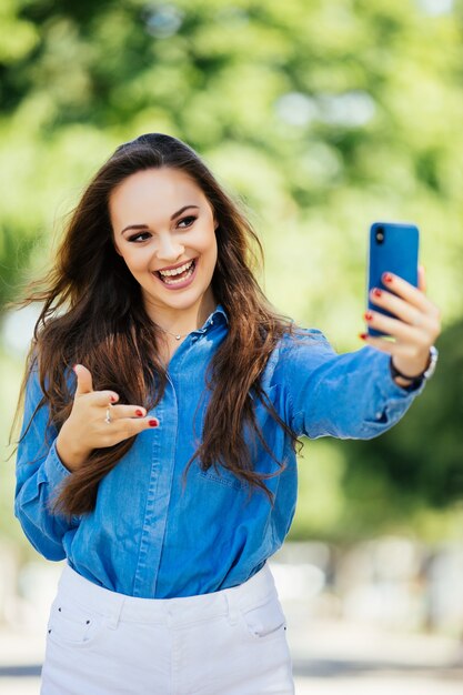 Young smiling girl making selfie wave on camera or make video call on the background of the city
