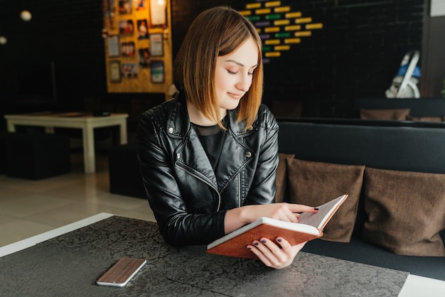 Young smiling girl reading book during the break in cafe