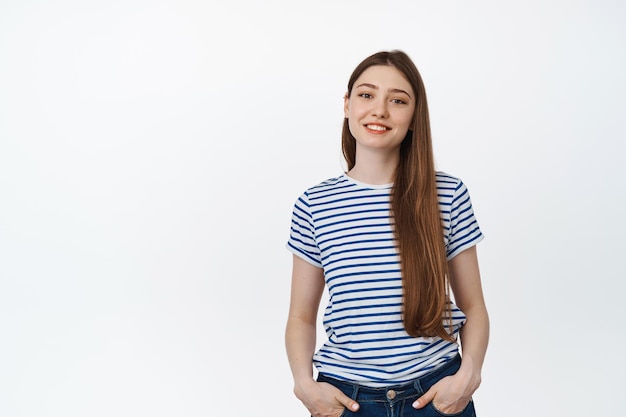 Young smiling girl in striped t-shirt. Happy teenager standing relaxed against white background.
