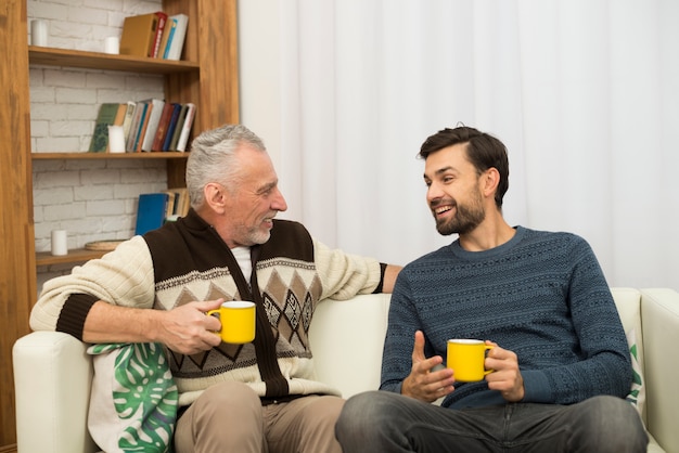 Молодой улыбающийся парень и старик с чашками на диване
