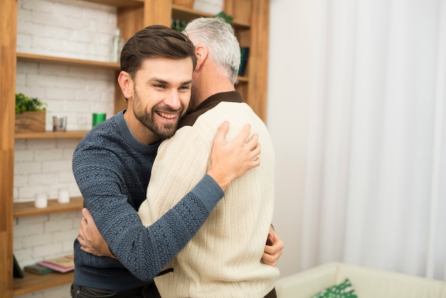 本棚の近くの老人とハグする若い微笑の男