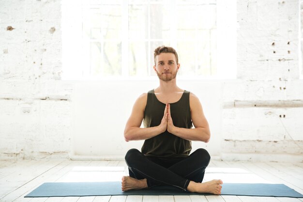 Young smiling guy sitting on a fitness mat and meditating