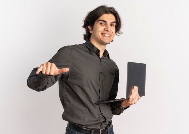 Young smiling handsome caucasian man holds and points at laptop isolated on white background with copy space