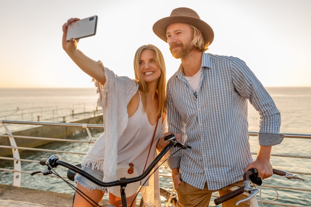 Молодой улыбающийся счастливый мужчина и женщина, путешествующие на велосипедах, делающие селфи на камеру телефона