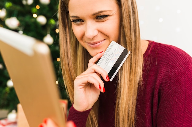 クリスマスツリーの近くにタブレットとプラスチックカードと若い笑顔の女性