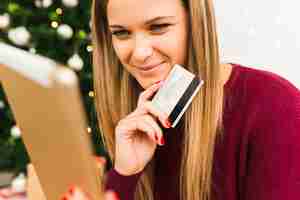 Free photo young smiling lady with tablet and plastic card near christmas tree