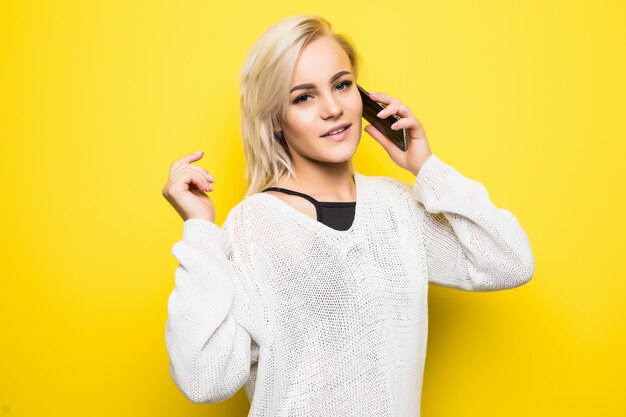 Young smiling lady woman girl in white sweater uses smartphone on yellow