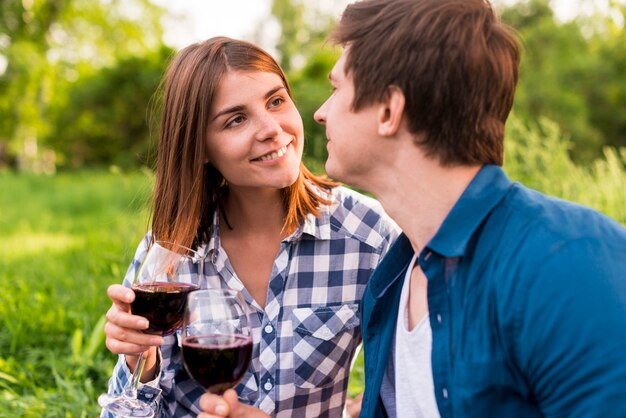 Молодые улыбающиеся любовники чокаются бокалом вина на улице