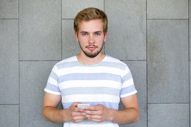 Young smiling male student holding mobile phone