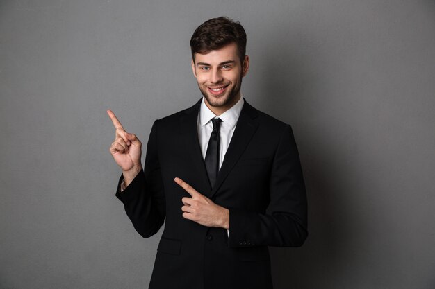 Young smiling man bearded businessman pointing with two finger upward, 