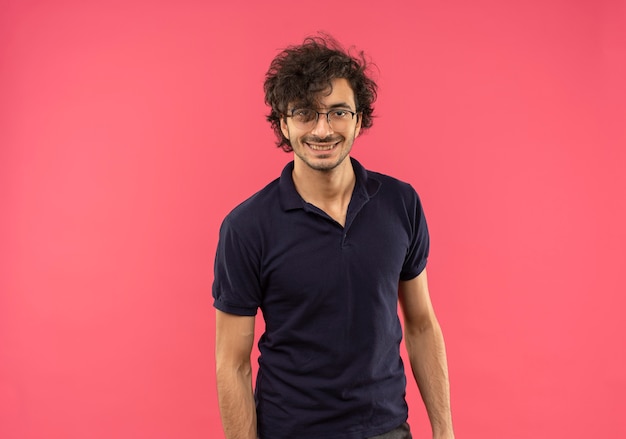 Young smiling man in black shirt with optical glasses looks isolated on pink wall