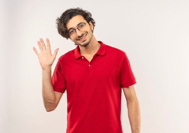 광학 안경 빨간 셔츠에 젊은 웃는 남자가 흰 벽에 고립 된 손을 제기