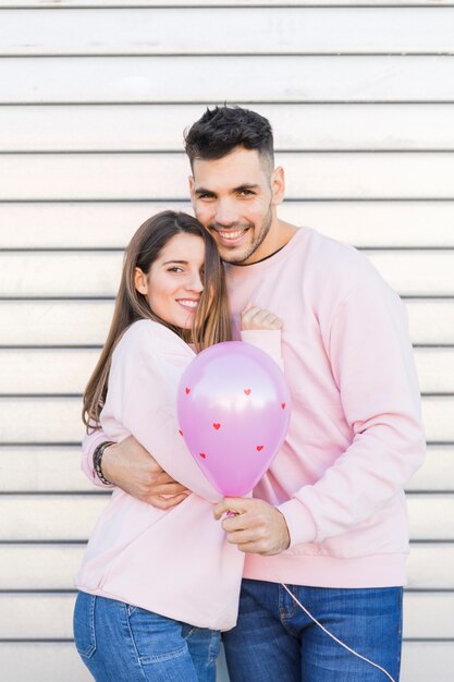 Young smiling man with balloon hugging attractive happy woman