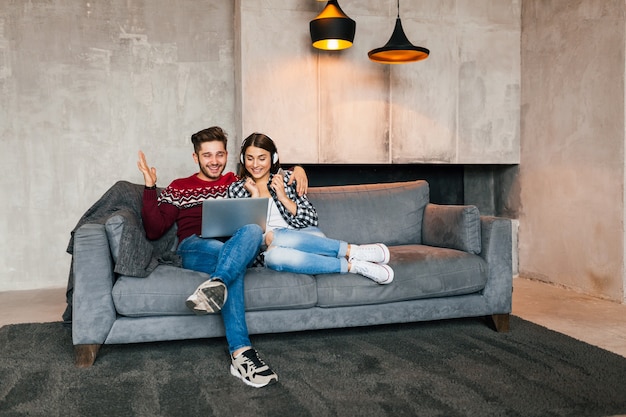 Young smiling man and woman sitting at home in winter looking in laptop with happy face expression, using internet, couple on leisure time together, positive emotion, dating