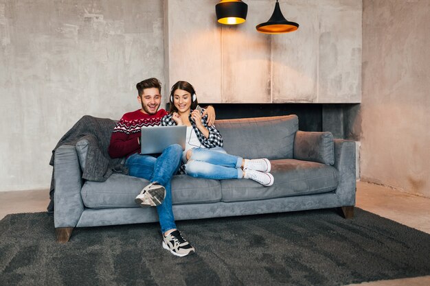 Young smiling man and woman sitting at home in winter looking in laptop with surprised exited face expression, using internet, couple on leisure time together, happy, positive emotion