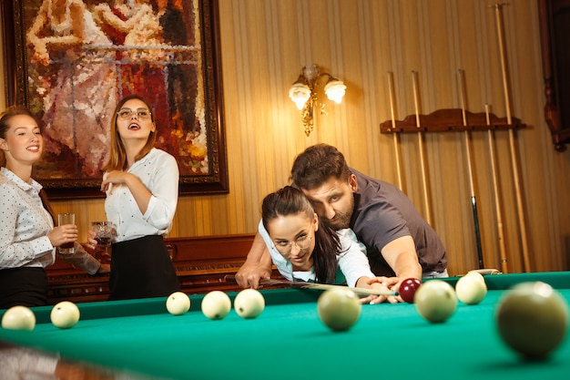 Young smiling men and women playing billiards at office or home after work. Business colleagues involving in recreational activity