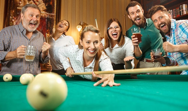 Free photo young smiling men and women playing billiards at office or home after work. business colleagues involving in recreational activity