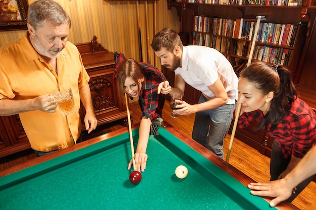 Young smiling men and women playing billiards at office or home after work.