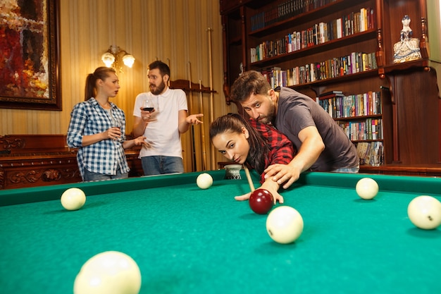 Young smiling men and women playing billiards at office or home after work.