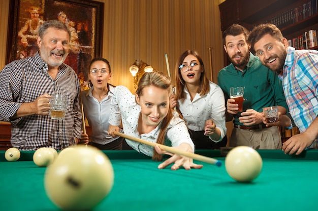 Young smiling men and women playing billiards at office or home after work.