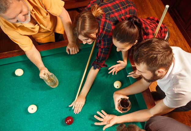 Young smiling men and women playing billiards at office or home after work.