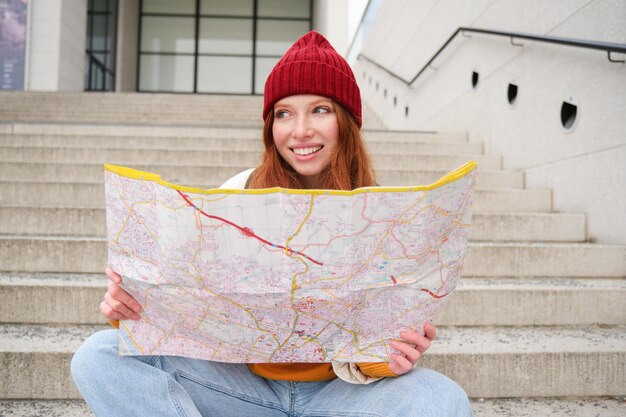 無料写真 若い笑顔の赤毛の女の子の観光客が屋外の階段に座り、市の紙の地図が方向を探している