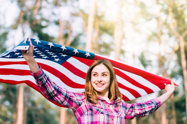 Молодая усмехаясь женщина нося флаг США на День независимости