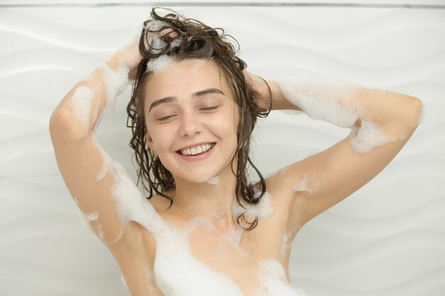 シャンプーで彼女の頭を洗って楽しむ若い笑顔の女性