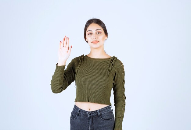 A young smiling woman in green sweater waving a hand.