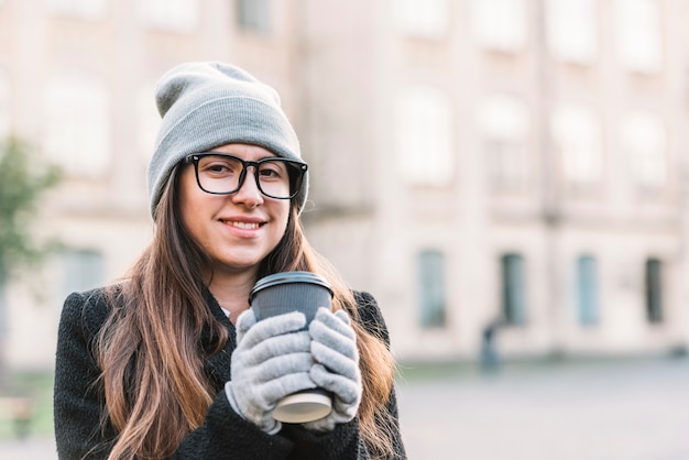 通りに飲み物のカップを保持している若い笑顔の女性