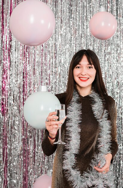 Young smiling woman holding glass near tinsel and decorative lamps 