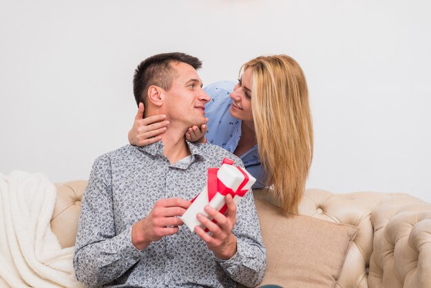 Young smiling woman looking at man with present on sofa