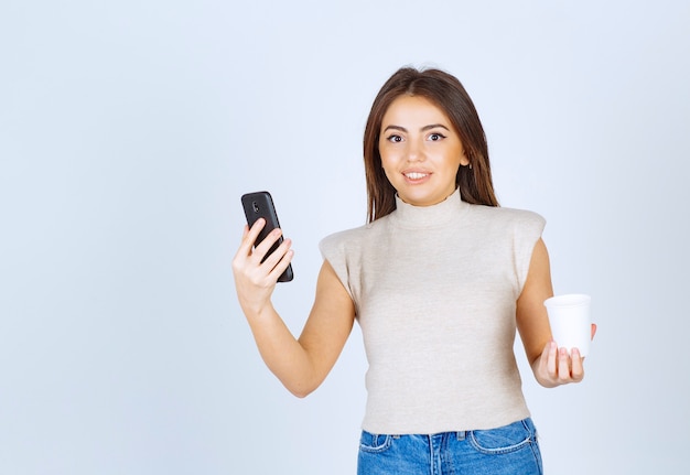 Un modello di giovane donna sorridente in possesso di un telefono e guardando la telecamera.