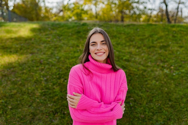 Молодая улыбающаяся женщина в розовом свитере гуляет в зеленом парке