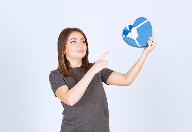 young smiling woman pointing at a heart shaped gift box.