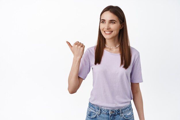 young smiling woman pointing left watching something aside on white.