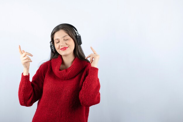 Молодая улыбающаяся женщина в красном теплом свитере слушает музыку в наушниках