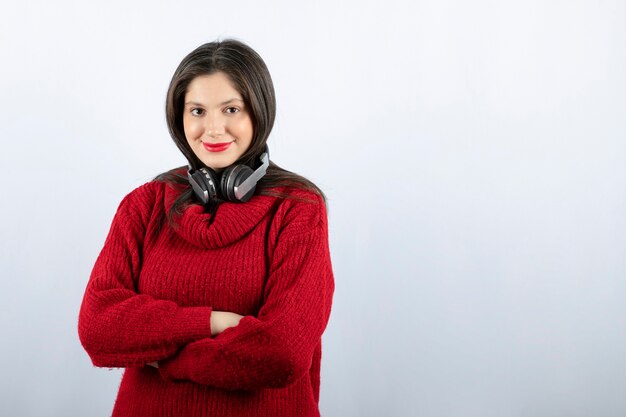 Молодая улыбающаяся женщина в красном теплом свитере стоит с наушниками
