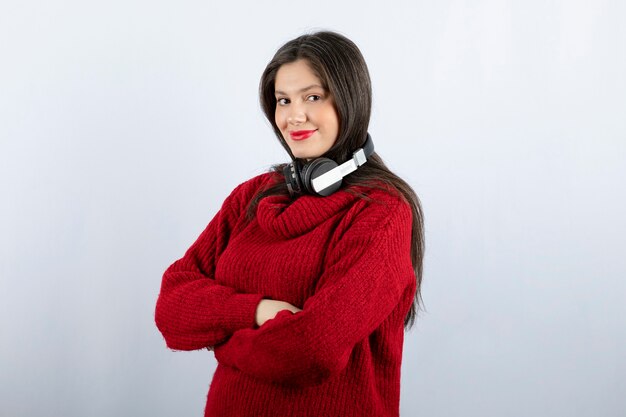 ヘッドフォンで立っている赤い暖かいセーターの若い笑顔の女性