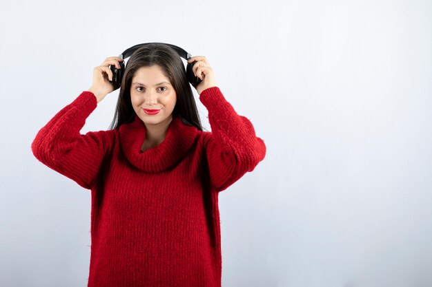 A young smiling woman in red warm sweater standing with headphones 