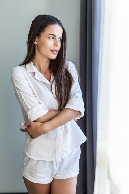 Young smiling woman relaxing at cozy home, feeling happy, resting in the morning, looking through the window