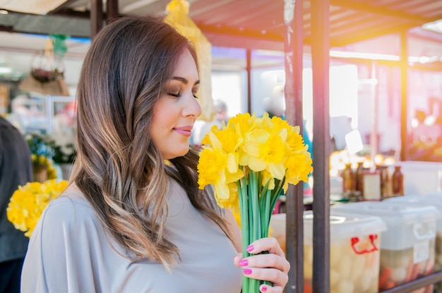 Young smiling woman selecting fresh flowers. Close up profile portrait of a beautiful and young woman enjoying and smelling a bouquet of flowers while standing in a fresh floral market stall during a sunny day outdoors.