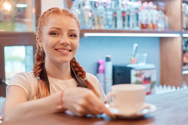 コーヒーショップのバーに立っている若い笑顔の女性