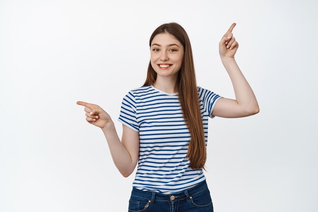 Young smiling woman suggest two options, pointing fingers up and left, showing variants, standing over white background