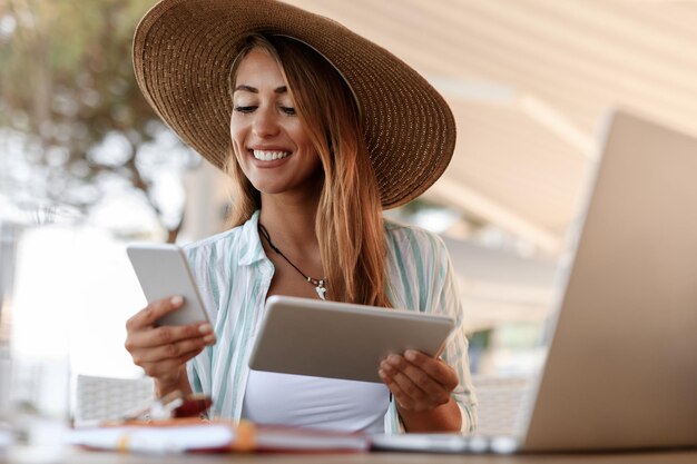 카페에서 휴대전화로 문자 메시지를 읽는 동안 디지털 태블릿을 사용하여 웃고 있는 젊은 여성