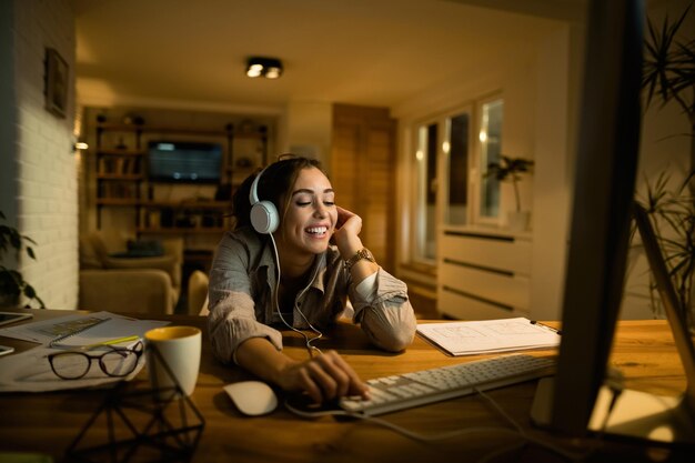 Young smiling woman with headphones surfing the Internet on a computer at night