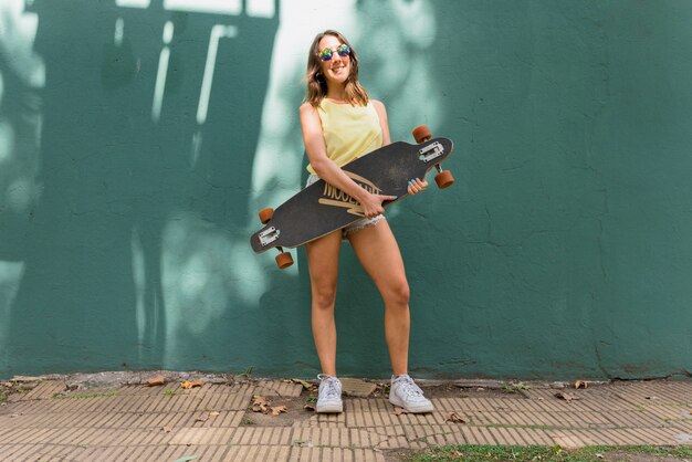 Young smiling woman with longboard against green wall