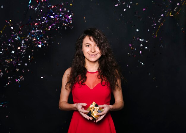 Free photo young smiling woman with present box between tossing confetti